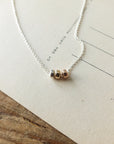 A delicate Three Things Necklace with three mixed metal beads displayed on a piece of paper by Becoming Jewelry.