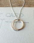 The Friendship Circles Necklace by Becoming Jewelry, featuring interlocking mixed metal pendants, is beautifully displayed on a postcard background.