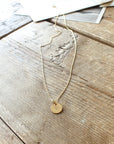 A Heart Necklace from Becoming Jewelry, featuring a small heart pendant, lies on a wooden surface. A few papers are partially visible in the background, adding to its significance as a truly meaningful gift.