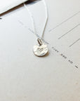 A Becoming Jewelry sterling silver Heart Necklace on a chain, resting on a piece of paper with printed text.
