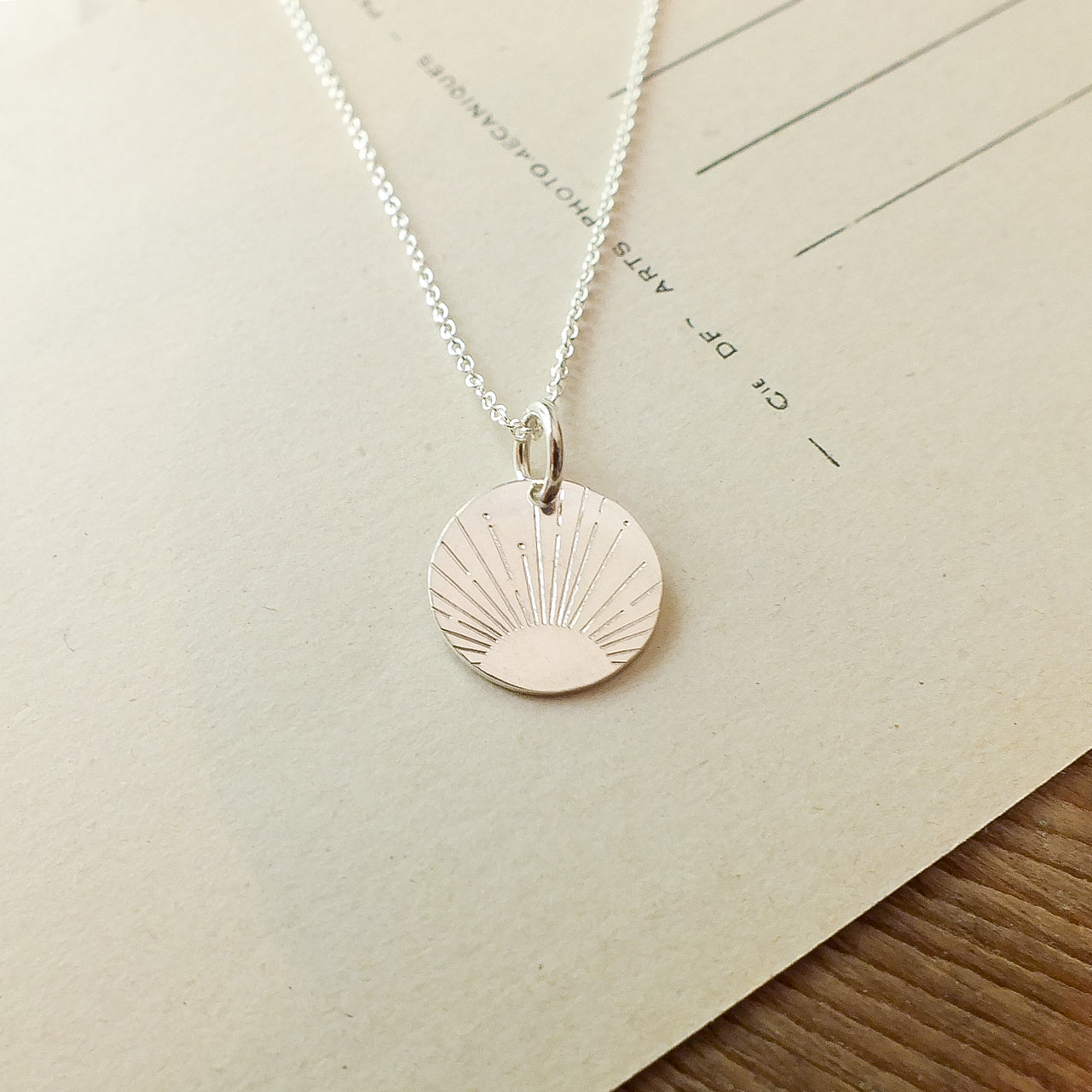 Becoming Jewelry&#39;s Irish Blessing Necklace with a sun charm design on a piece of paper.