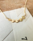 A close-up of the delicate Becoming Jewelry Mothers & Daughters Necklace, featuring a chain of small, linked heart-shaped charms, beautifully laid on a cream-colored envelope on a wooden surface. This necklace makes the perfect gift of connection for that special woman in your life.
