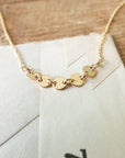 Close-up of the Becoming Jewelry Mothers & Daughters Necklace with small circular links laid on a white envelope, placed on a wooden surface—perfect for celebrating the bond between mothers and daughters.