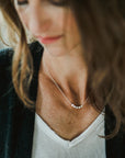 Close-up of a person wearing a black cardigan, white shirt, and a silver Mothers & Daughters Necklace from Becoming Jewelry with multiple small beads, looking down slightly.