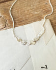 A silver Becoming Jewelry Mothers & Daughters Necklace, featuring small, linked circular discs, is elegantly placed on a piece of white paper atop a wooden surface, providing a beautiful gift symbolizing connection.