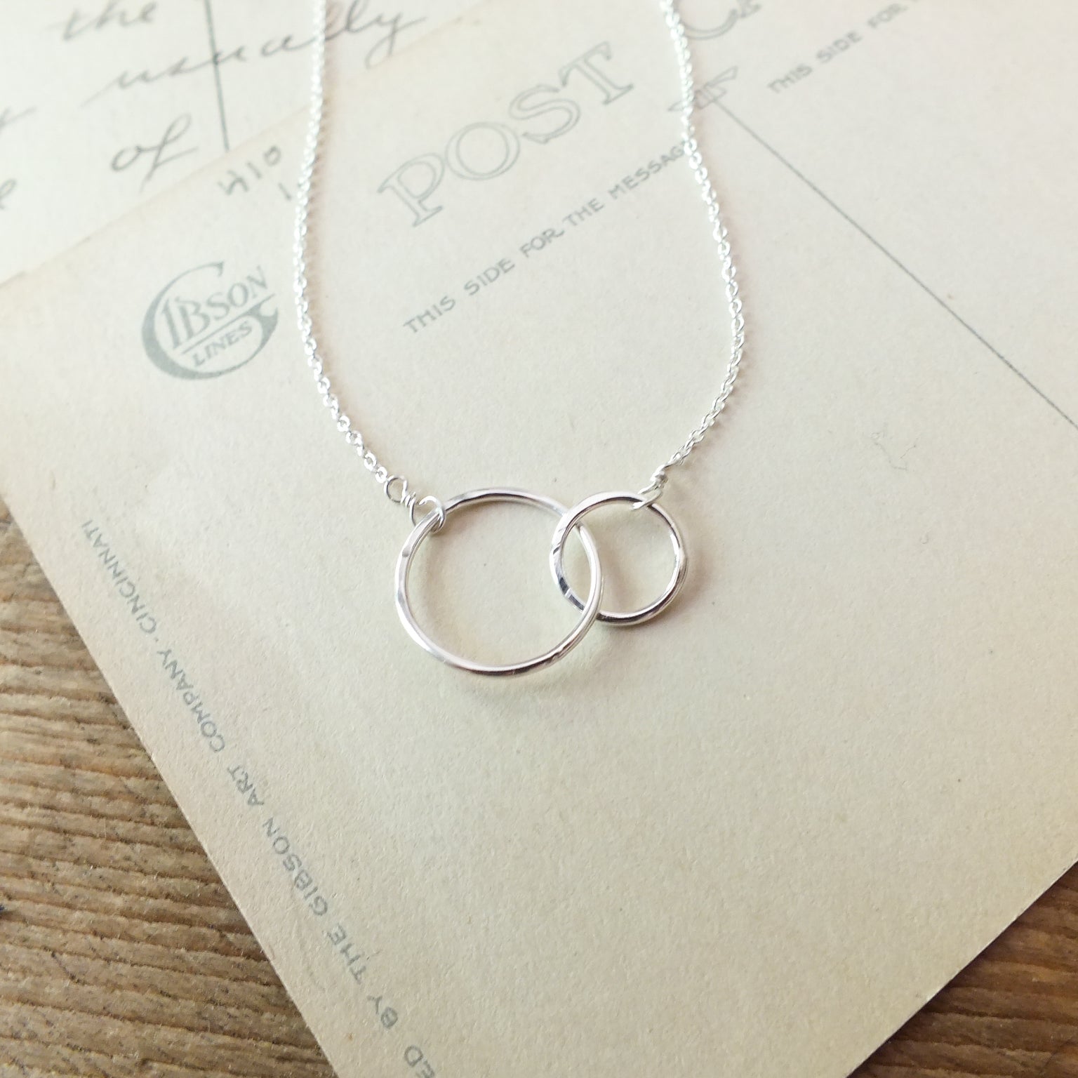 Silver interlocked circles pendant necklace, a perfect Becoming Jewelry mother&#39;s necklace, displayed on a vintage postcard.