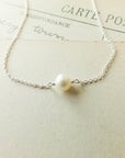 The Simple Pleasures Pearl Necklace by Becoming Jewelry is a delicate silver piece featuring a single pearl pendant, perfectly embodying timeless beauty against vintage-style postcards.