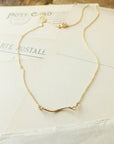 A delicate Path Necklace from Becoming Jewelry, featuring a small curved bar pendant, is laid on top of a white envelope with partially visible text and postage marks—a meaningful gift for those following their heart.
