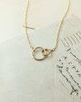 The Sisters Necklace by Becoming Jewelry, a delicate gold piece featuring intertwined circles, rests gracefully on a stack of antique papers adorned with handwritten text, making it the ideal sister gift.