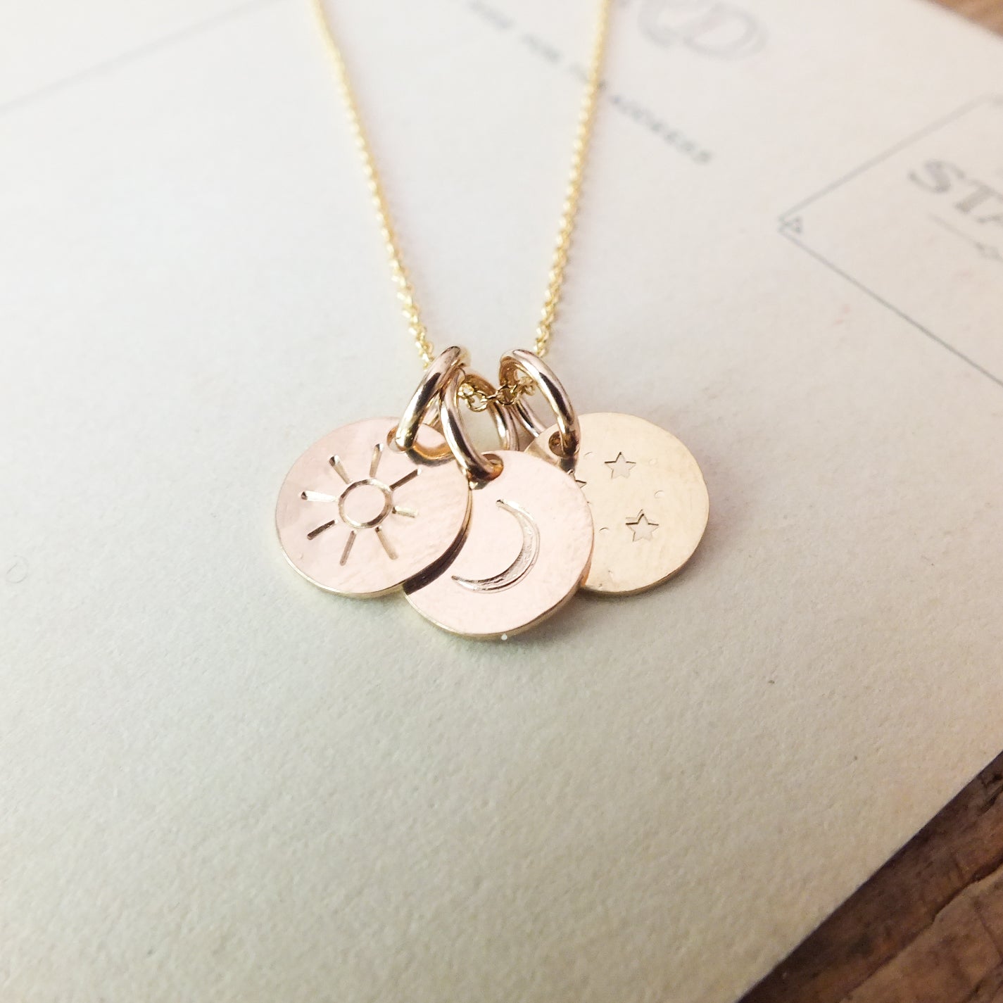 Becoming Jewelry&#39;s Gold-filled Sun Moon and Stars Necklace on wooden surface.
