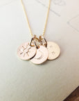 The Sun Moon and Stars Necklace by Becoming Jewelry features four small, round pendants engraved with a sun charm, a crescent moon, two stars, and another crescent moon. The necklace is beautifully displayed on a light-colored surface.