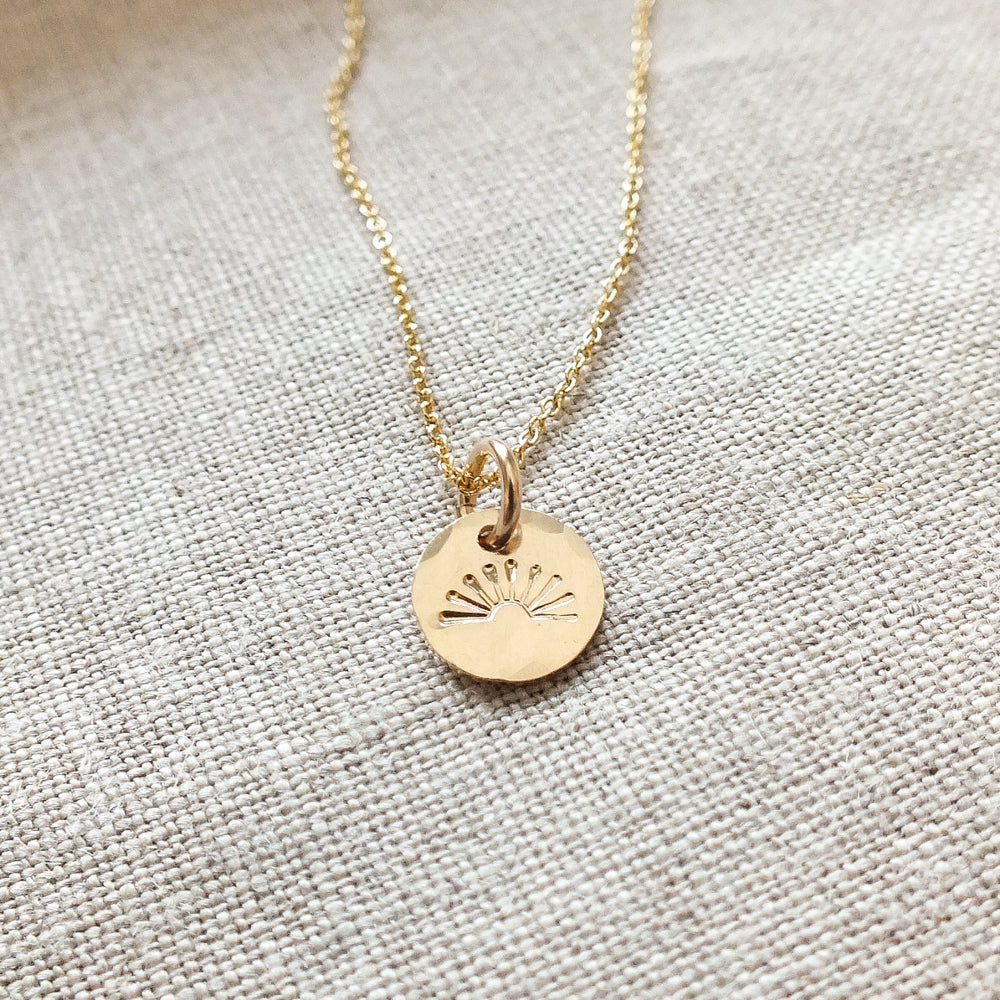 You Are My Sunshine Necklace&quot; by Becoming Jewelry, featuring a sunshine charm, lying on a textured fabric surface.