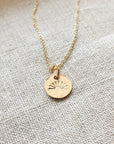 You Are My Sunshine Necklace" by Becoming Jewelry, featuring a sunshine charm, lying on a textured fabric surface.