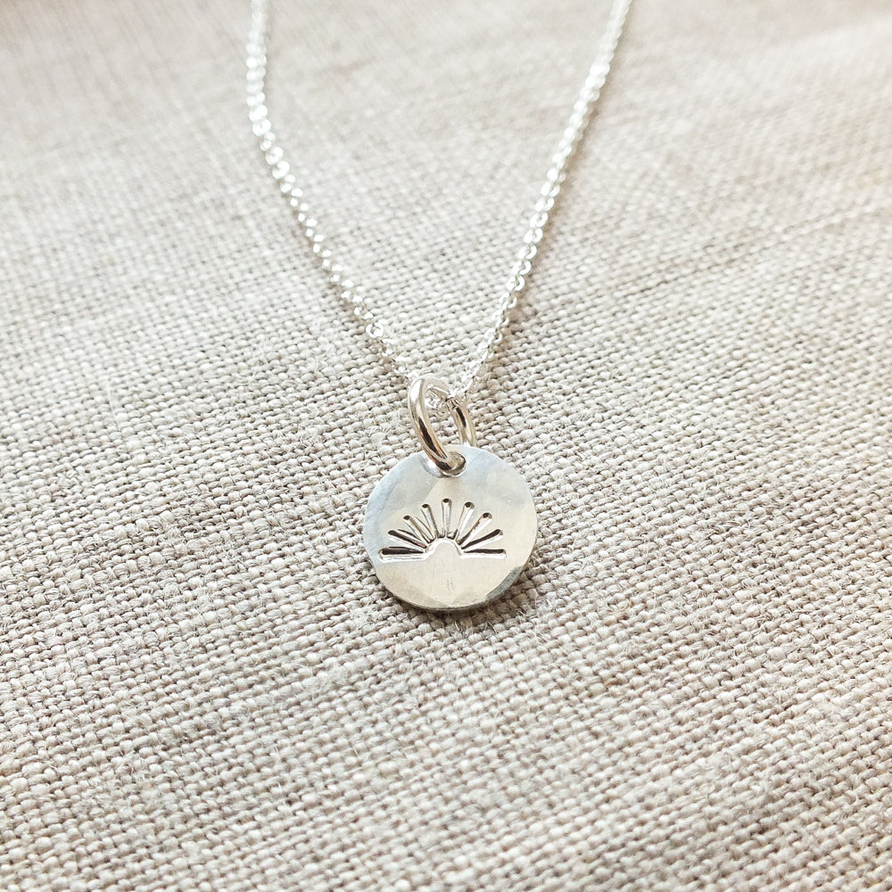 Becoming Jewelry&#39;s You Are My Sunshine Necklace features a sterling silver pendant with a Sunshine Charm design on a textured fabric surface.
