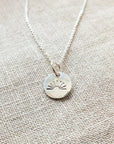 Becoming Jewelry's You Are My Sunshine Necklace features a sterling silver pendant with a Sunshine Charm design on a textured fabric surface.