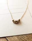 My Wish For You Necklace by Becoming Jewelry with a curved bar pendant on a wooden surface.