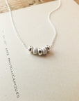The My Wish For You Necklace by Becoming Jewelry features five small, round beads and is showcased on a beige background. It makes for a perfect gift that embodies the essence of Ralph Waldo Emerson's quote, "The only gift is a portion of thyself.