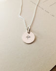 Close-up of the Light Within Necklace by Becoming Jewelry, a silver piece featuring a tiny starburst pendant, serving as a daily reminder of the light within, placed on a beige background.
