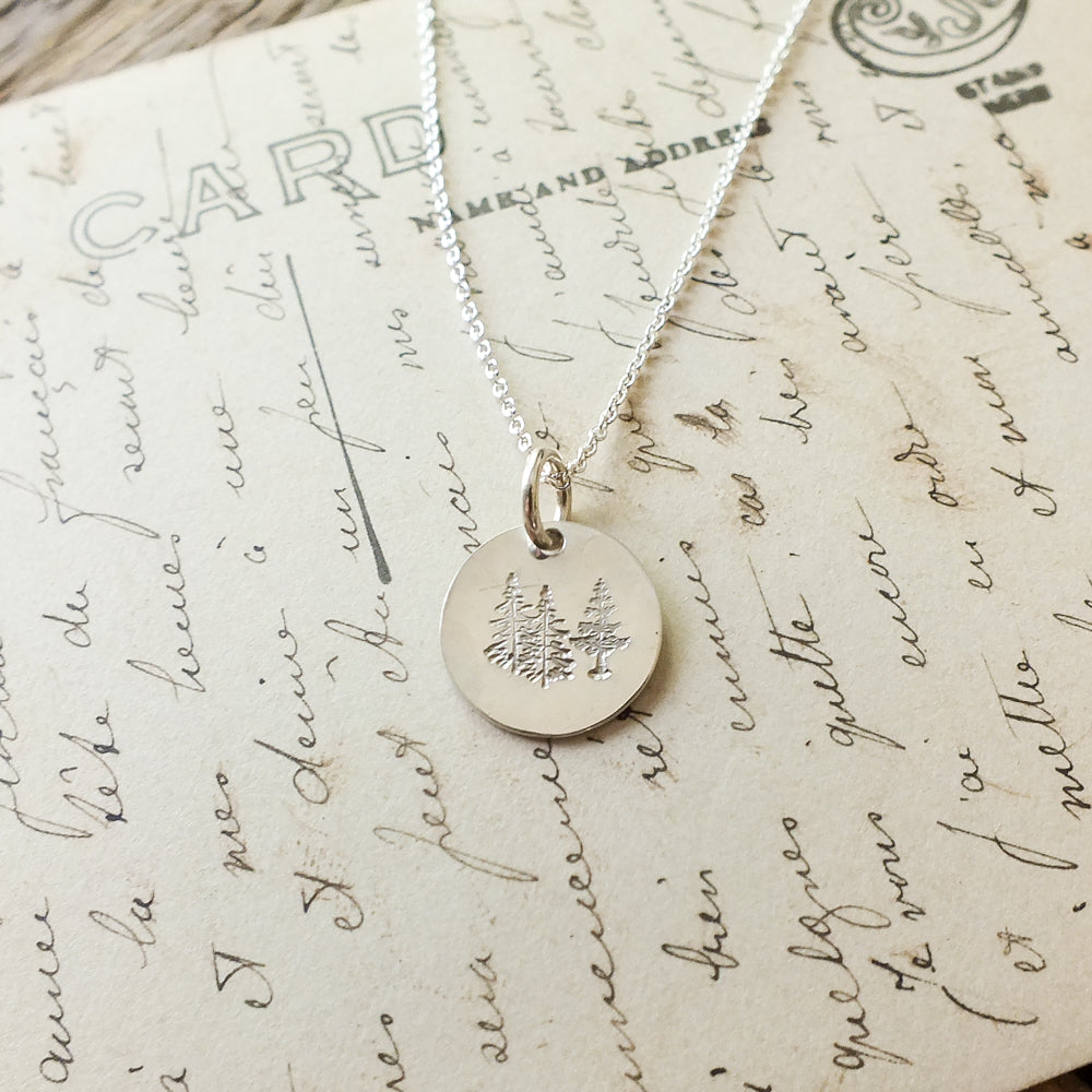 Becoming Jewelry&#39;s Trees Necklace with a trees charm pendant displayed on a background of handwritten text.