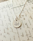 The Trees Necklace from Becoming Jewelry, a silver necklace adorned with a circular pendant featuring an engraved tree design, is elegantly placed on a vintage handwritten letter, capturing the essence of nature's restoration.
