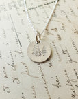 A Trees Necklace from Becoming Jewelry, featuring a round silver pendant engraved with nature's trees, is placed atop a handwritten letter, invoking thoughts of restoration.
