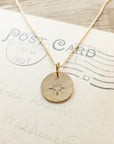 A North Star Necklace from Becoming Jewelry, featuring a round pendant engraved with a star design, is carefully placed on an old postcard dated from 1907, making it a perfect gift for travelers.