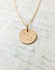 Watch the Stars Necklace pendant with star and moon cutouts on a chain, displayed on a marble surface by Becoming Jewelry.