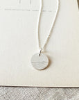 The Sea Necklace pendant with waves charm design on a chain, displayed on a card by Becoming Jewelry.