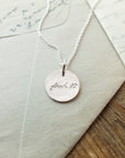 Becoming Jewelry's Fuck It Necklace with handwritten inscription on wooden background with envelopes.