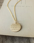 The "Strong Women Necklace" by Becoming Jewelry, featuring a gold round charm pendant resting on a piece of paper, makes for a thoughtful gift perfect for daily wear.