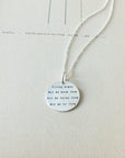 Becoming Jewelry's Strong Women Necklace with a charm inscribed with a message about strong women displayed on a piece of paper.