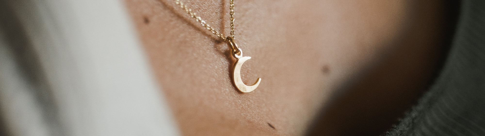 Close-up of a golden crescent moon pendant on a necklace resting against a person's neck.