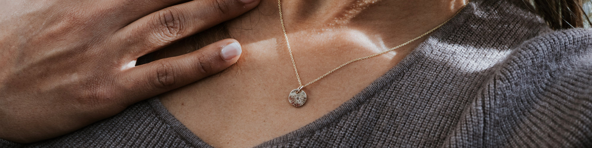 Close-up of a necklace with a small, oval pendant on a woman wearing a gray tank top, focused on the chest area with a blurred background.