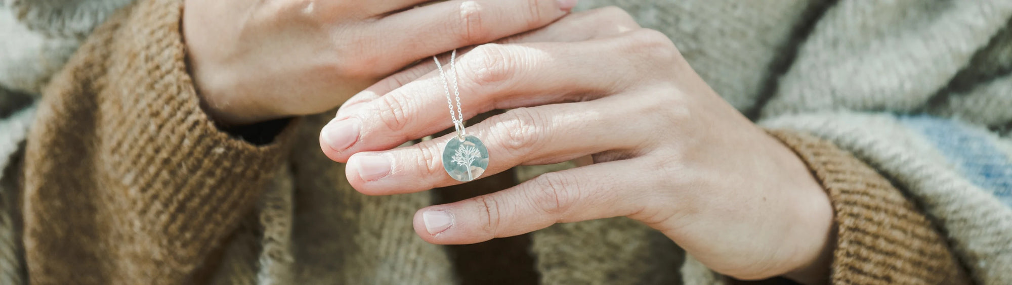 Hands holding a silver necklace with a clear gem pendant, close-up view.