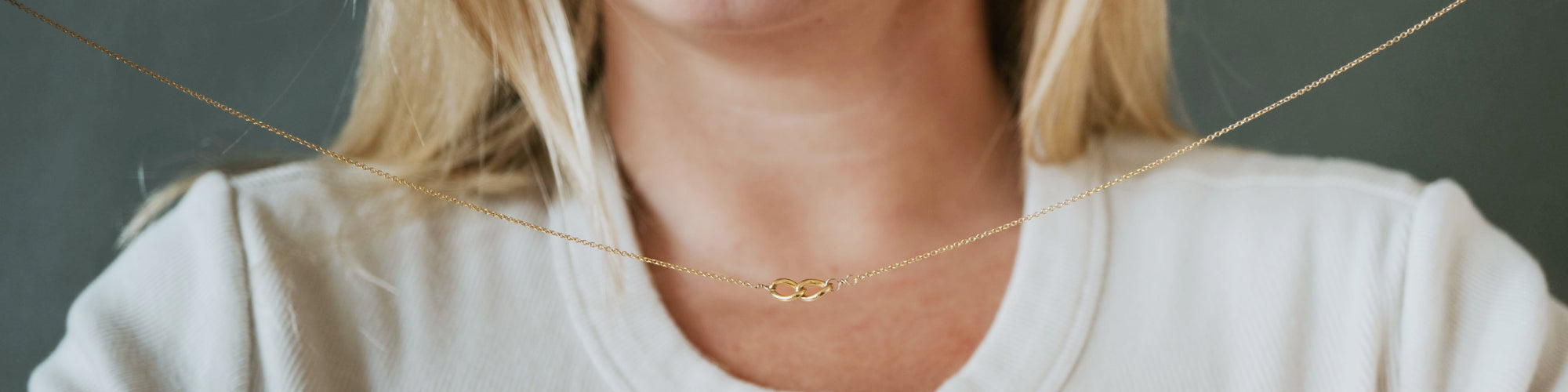 Hands holding a silver necklace with a clear gem pendant, close-up view.