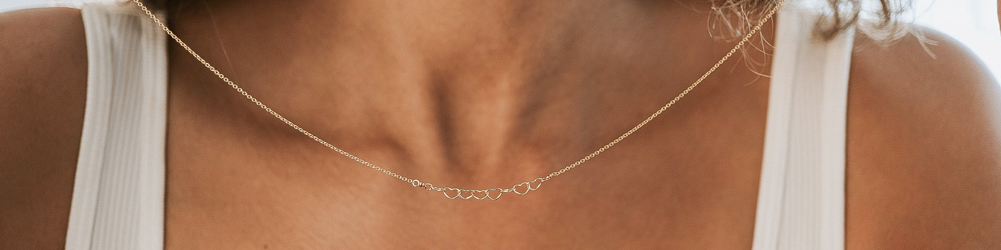 Close-up of a person wearing a beige knit sweater and a geometric gold necklace.