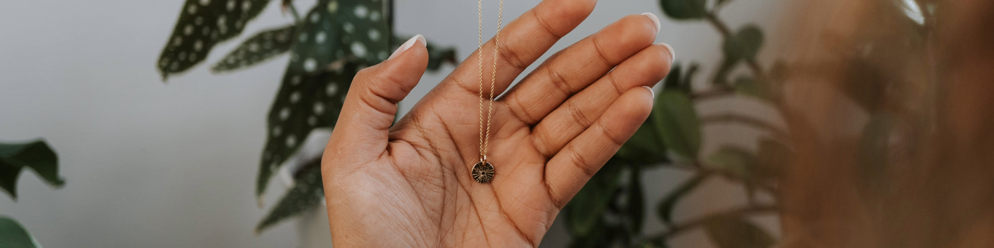 Close-up of a woman's neck wearing a delicate gold necklace with a small pendant, contrasted against her white sweater and dark hair.