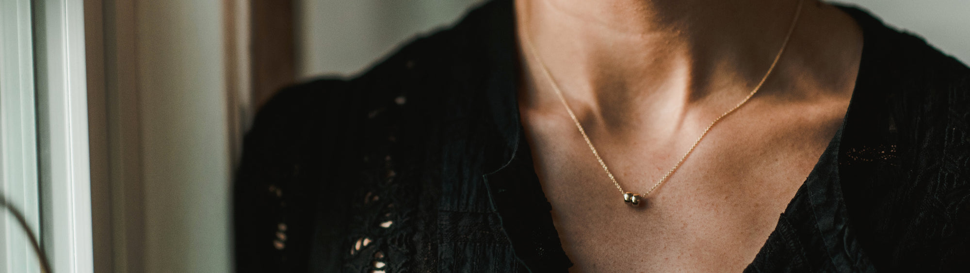 Close-up of a person wearing a delicate gold necklace with a small pendant, focusing on the necklace and the neckline of a black lace outfit.