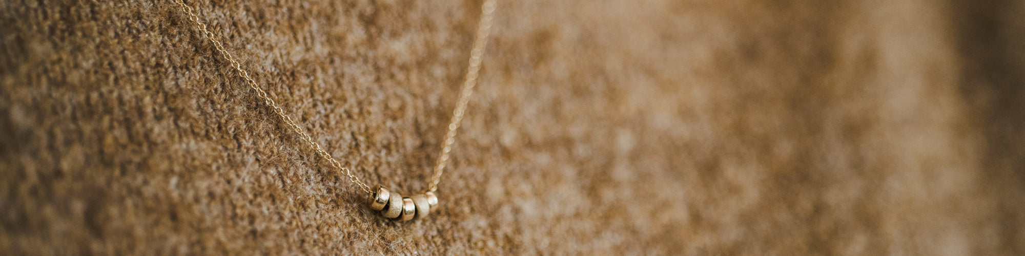Necklace with small beads on a model wearing a tan sweater 