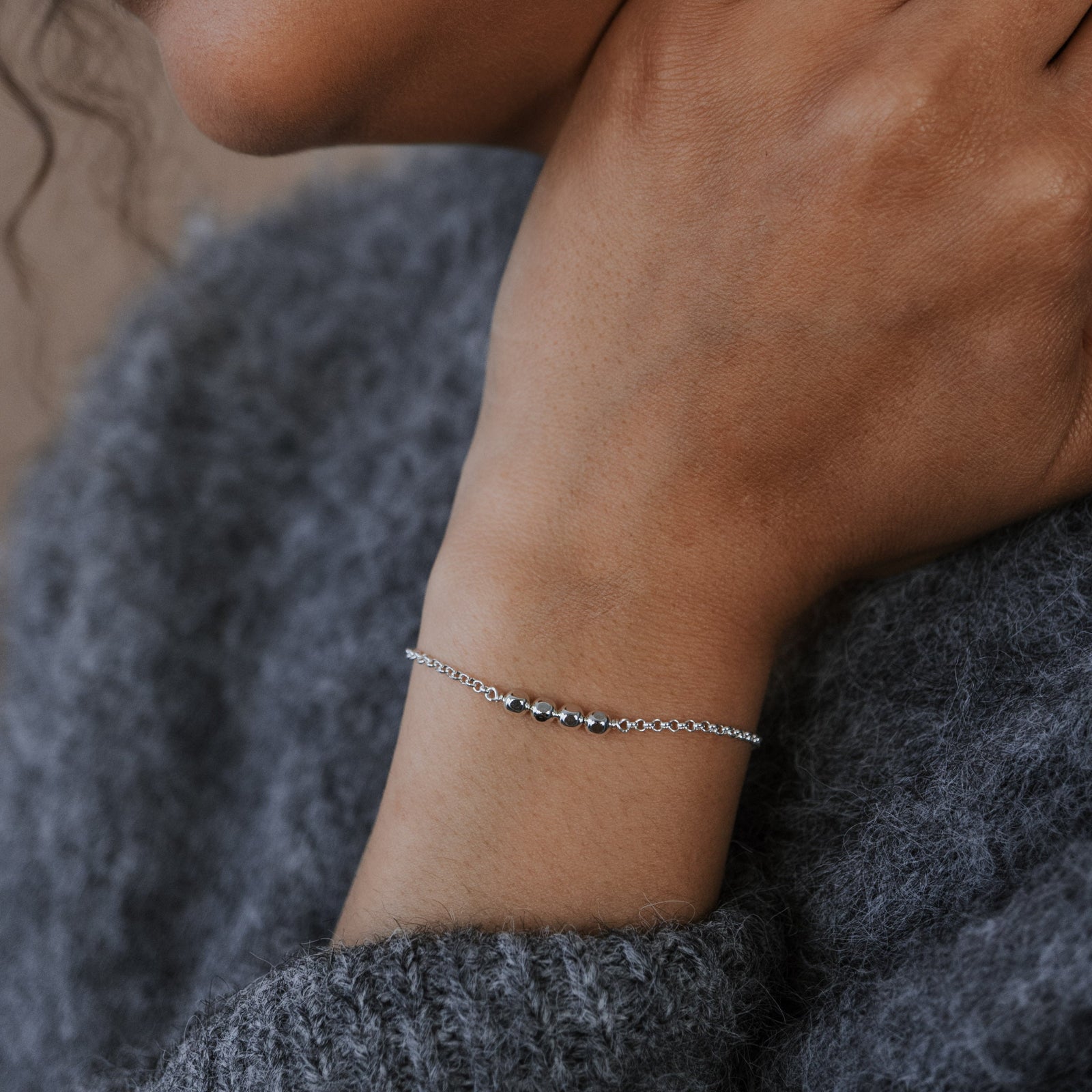 Close-up of a person wearing a bracelet on a gray sweater
