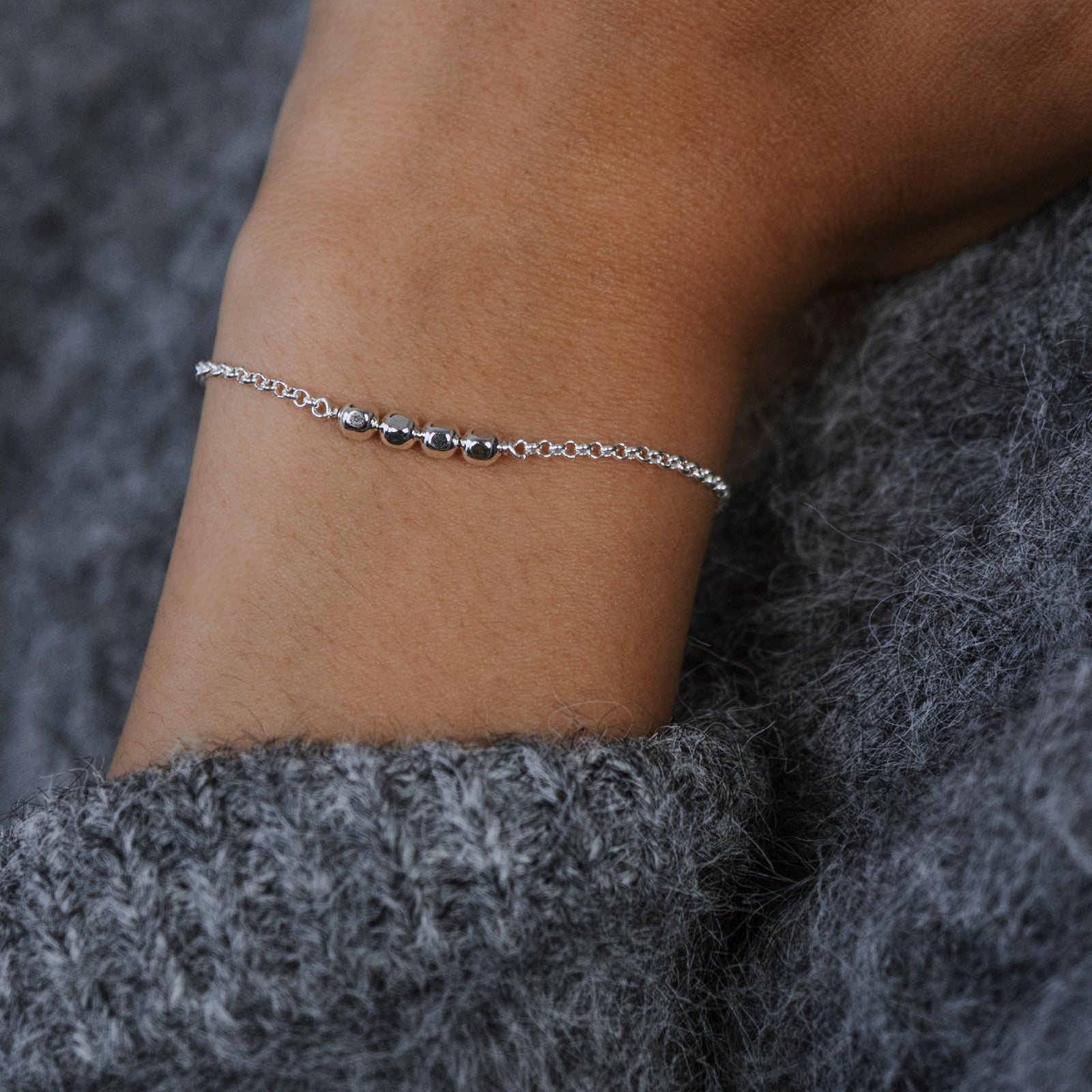 Close-up of a wrist wearing a silver bracelet with a textured gray sweater sleeve.