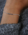 Close-up of a wrist wearing a silver bracelet with a textured gray sweater sleeve.