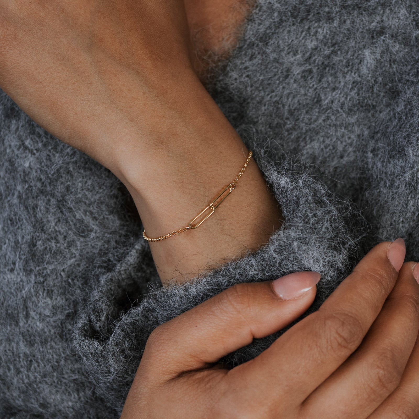 Close-up of a hand wearing a gold bracelet on a gray fabric background