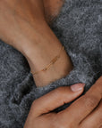 Close-up of a hand wearing a gold bracelet on a gray fabric background