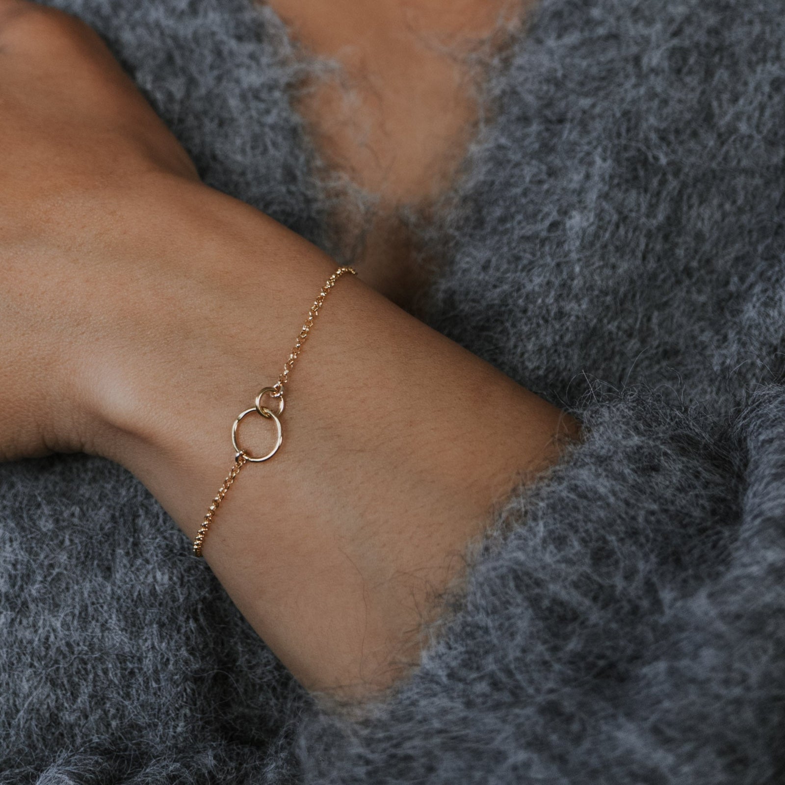 Woman wearing a gold bracelet and earrings, with a neutral background