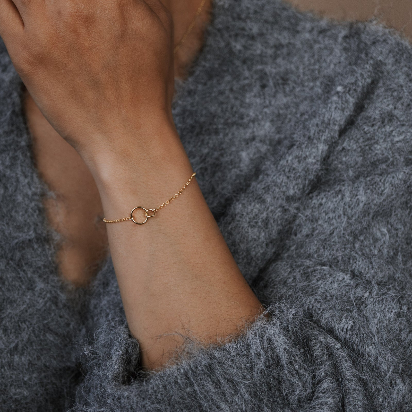 Person wearing a gold bracelet on a gray sweater