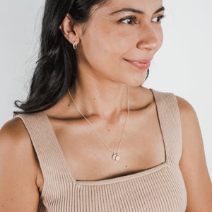 Woman wearing a beige top and a Count My Blessings Necklace by Becoming Jewelry, looking to the side.