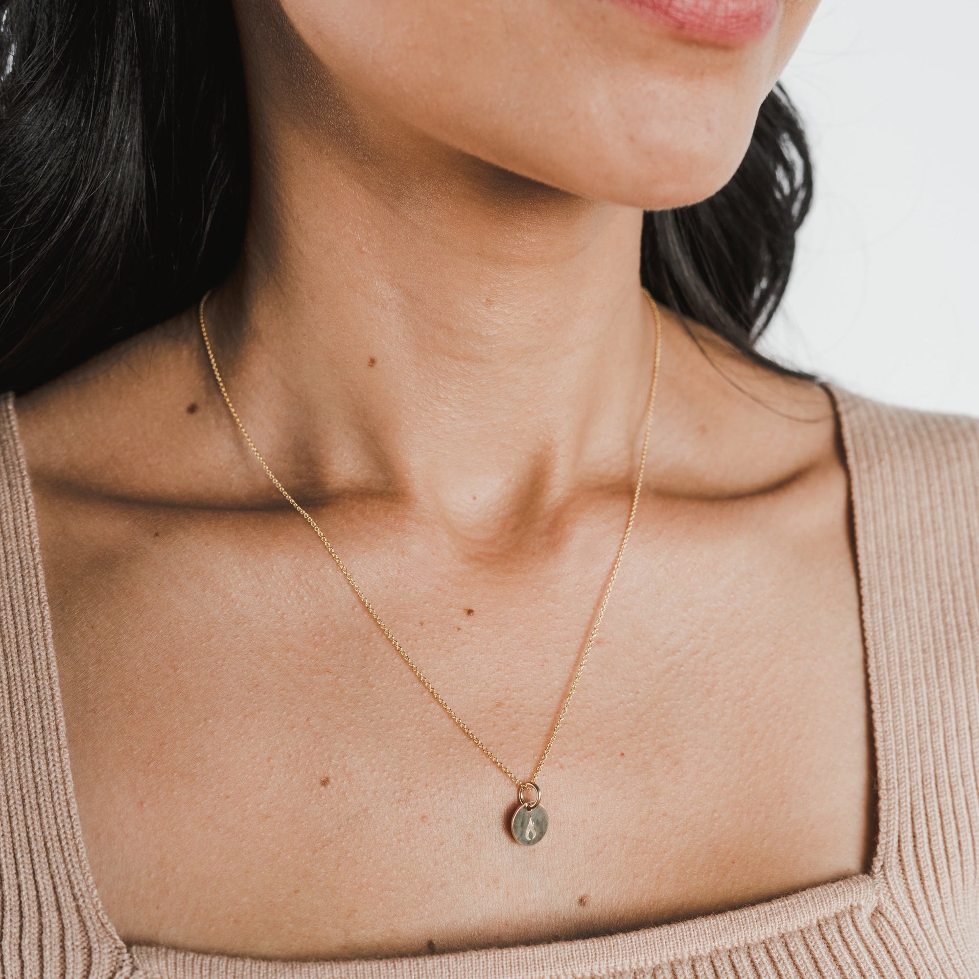 Close-up of a woman wearing the On Fire Necklace by Becoming Jewelry, featuring a small round pendant. She is dressed in a beige ribbed top against a plain white background, making this piece an ideal gift for graduates looking for inspiration.