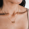 A woman wearing a Linked By Blood Necklace by Becoming Jewelry with a heart-shaped pendant.