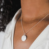Close-up of a woman wearing a Becoming Jewelry Strong Women Necklace with a round pendant inscribed with text.